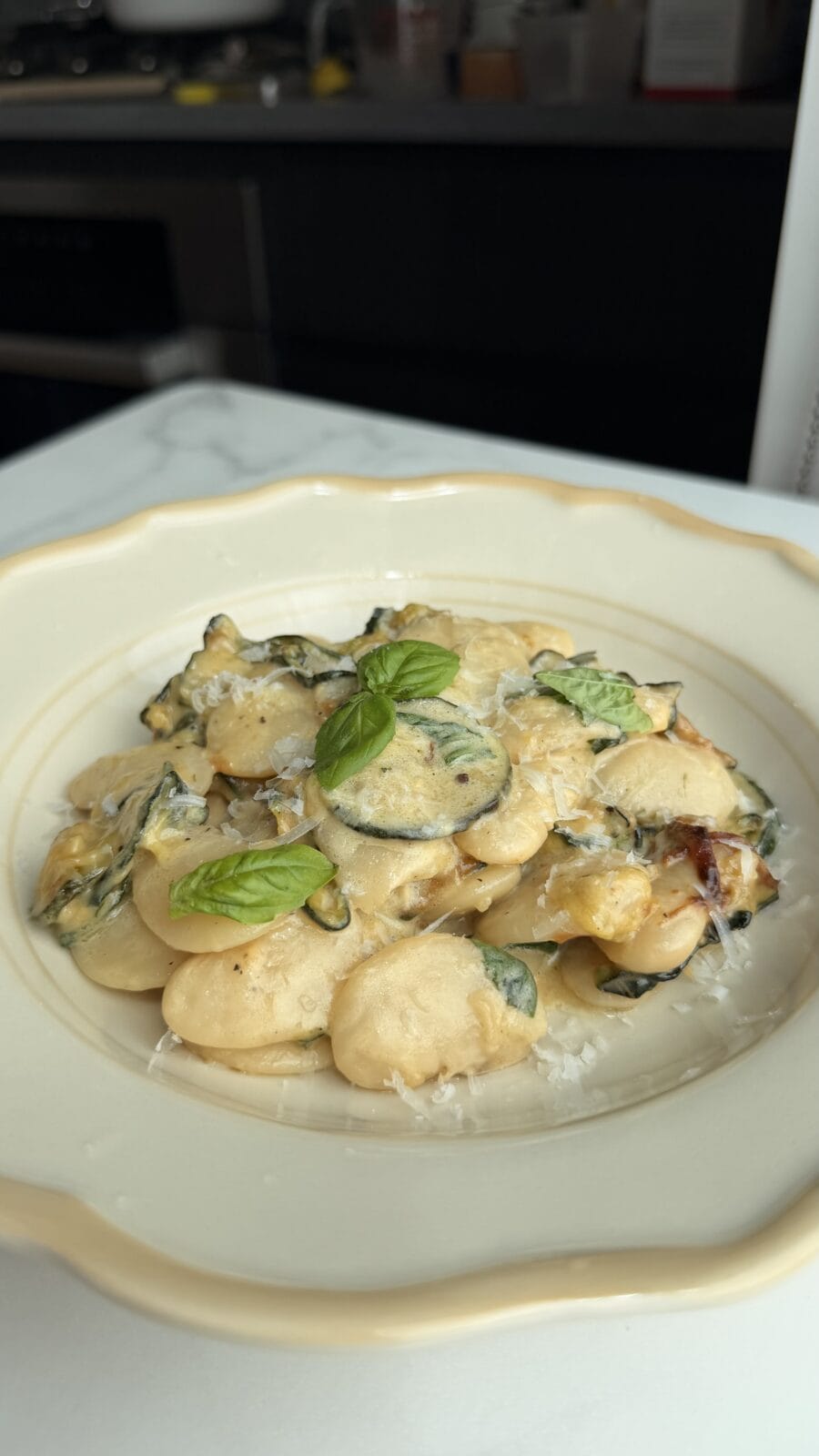 A plate of beans with creamy sauce, basil, zucchini, grated cheese, and basil leaves, served on a white dish.