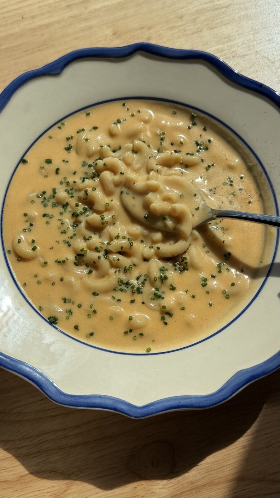 A bowl of macaroni and cheese garnished with chopped chives, with a spoon resting inside.