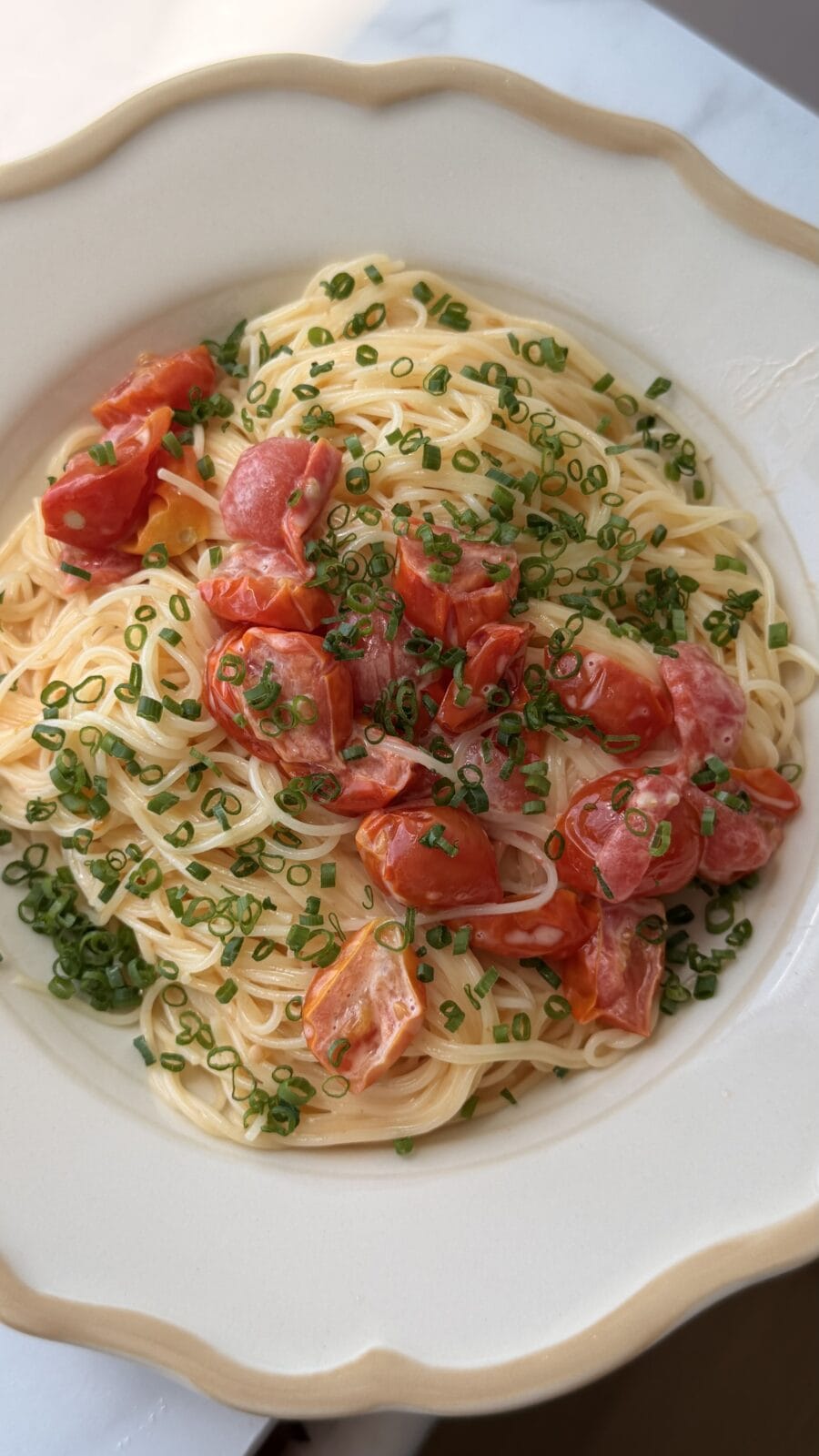 A plate of spaghetti topped with halved cherry tomatoes and chopped chives, served in a white bowl.