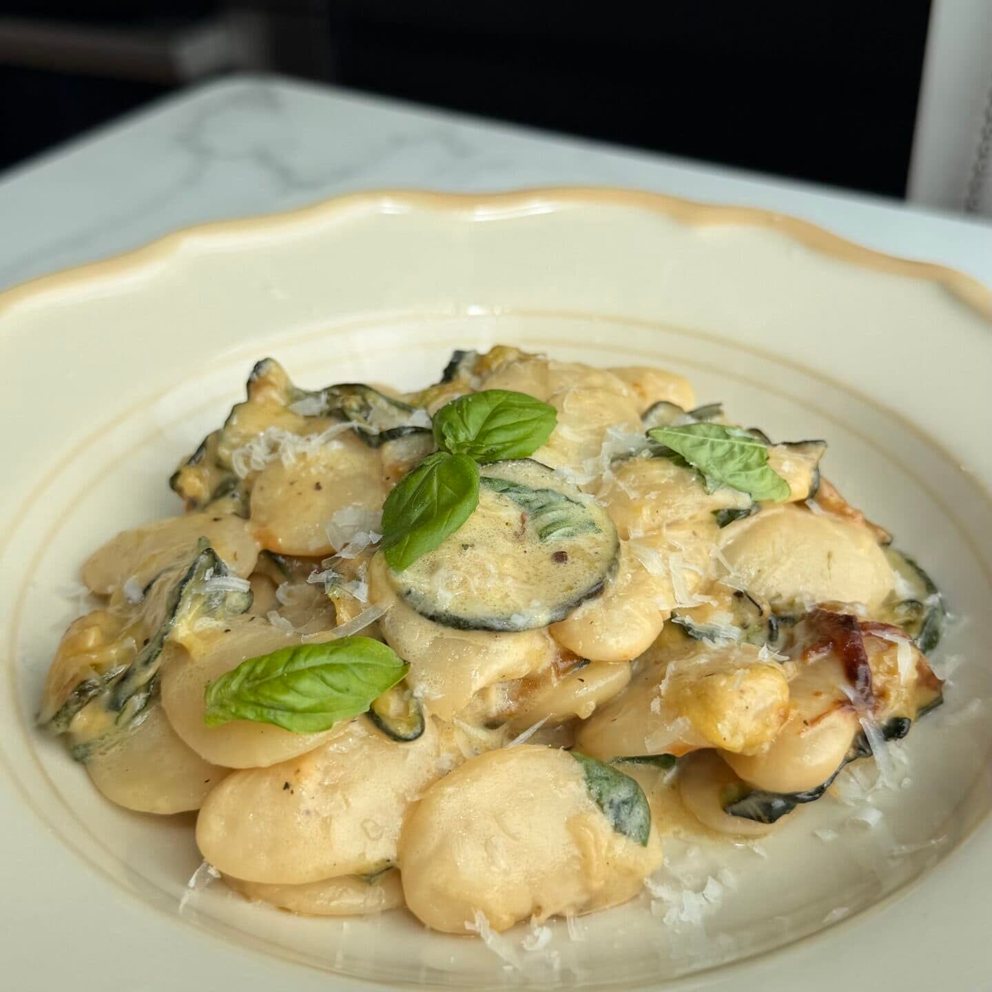 A plate of beans with creamy sauce, basil, zucchini, grated cheese, and basil leaves, served on a white dish.
