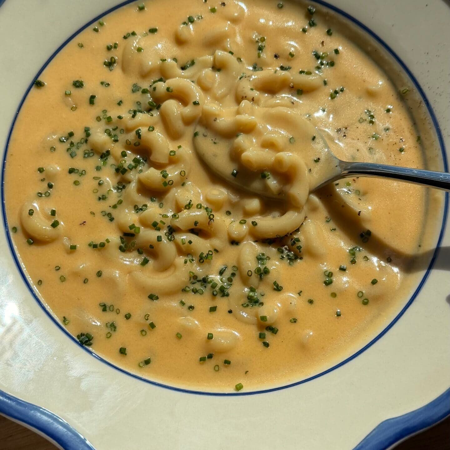 A bowl of macaroni and cheese garnished with chopped chives, with a spoon resting inside.