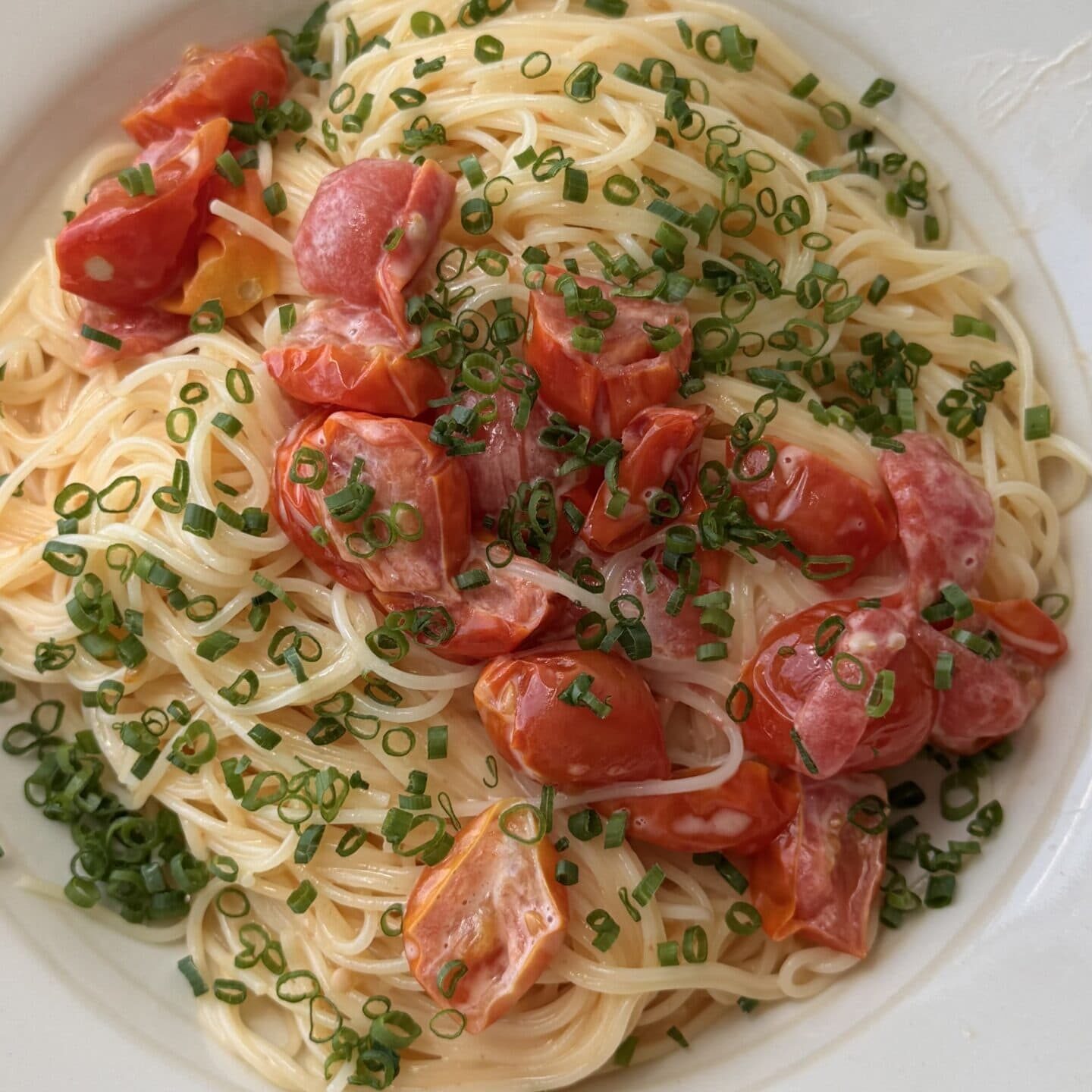 A plate of spaghetti topped with halved cherry tomatoes and chopped chives, served in a white bowl.