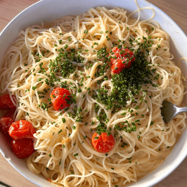 A bowl of thin spaghetti topped with chopped chives and cherry tomatoes, with a fork resting on the side of the bowl.