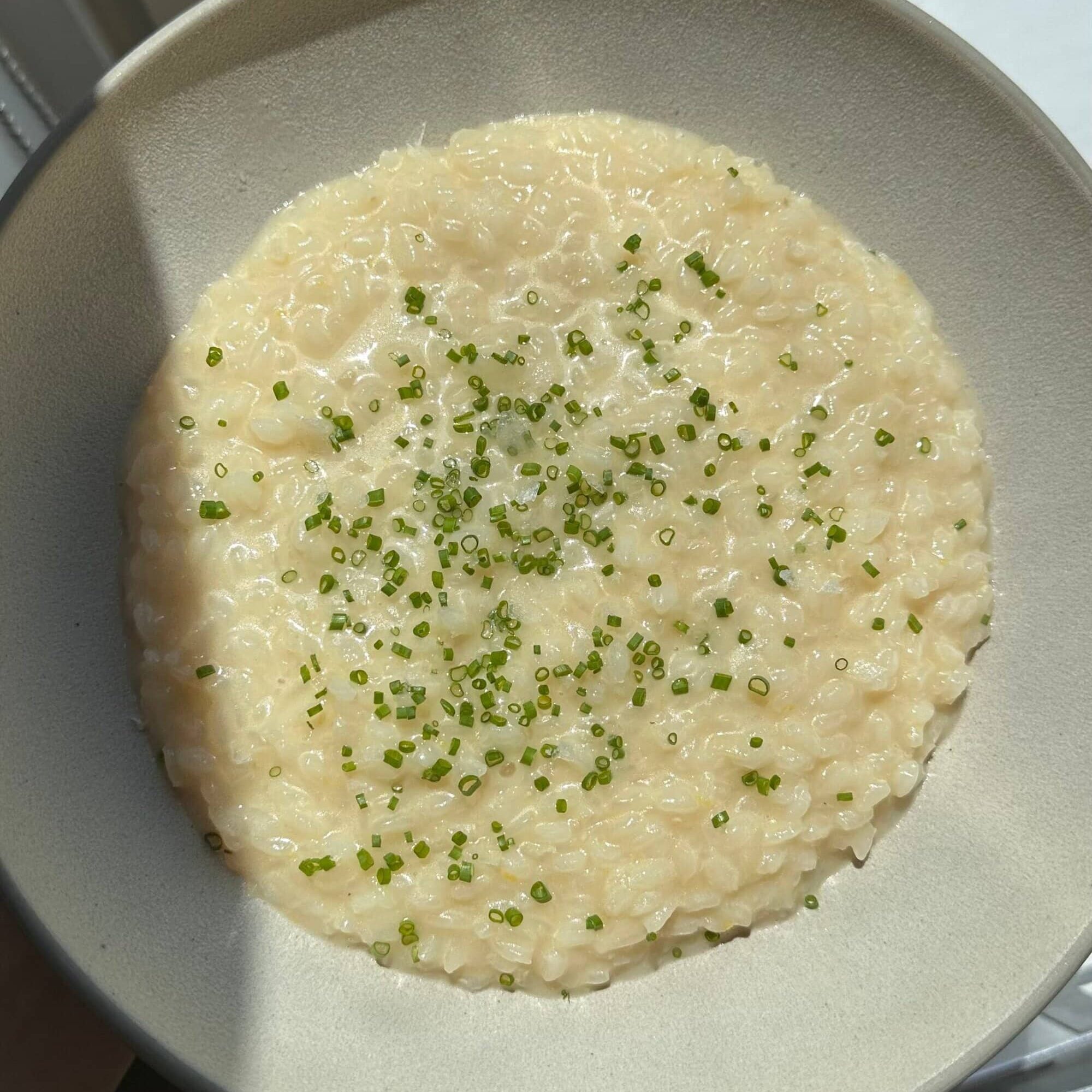 A bowl of creamy risotto topped with finely chopped chives, photographed in natural light.