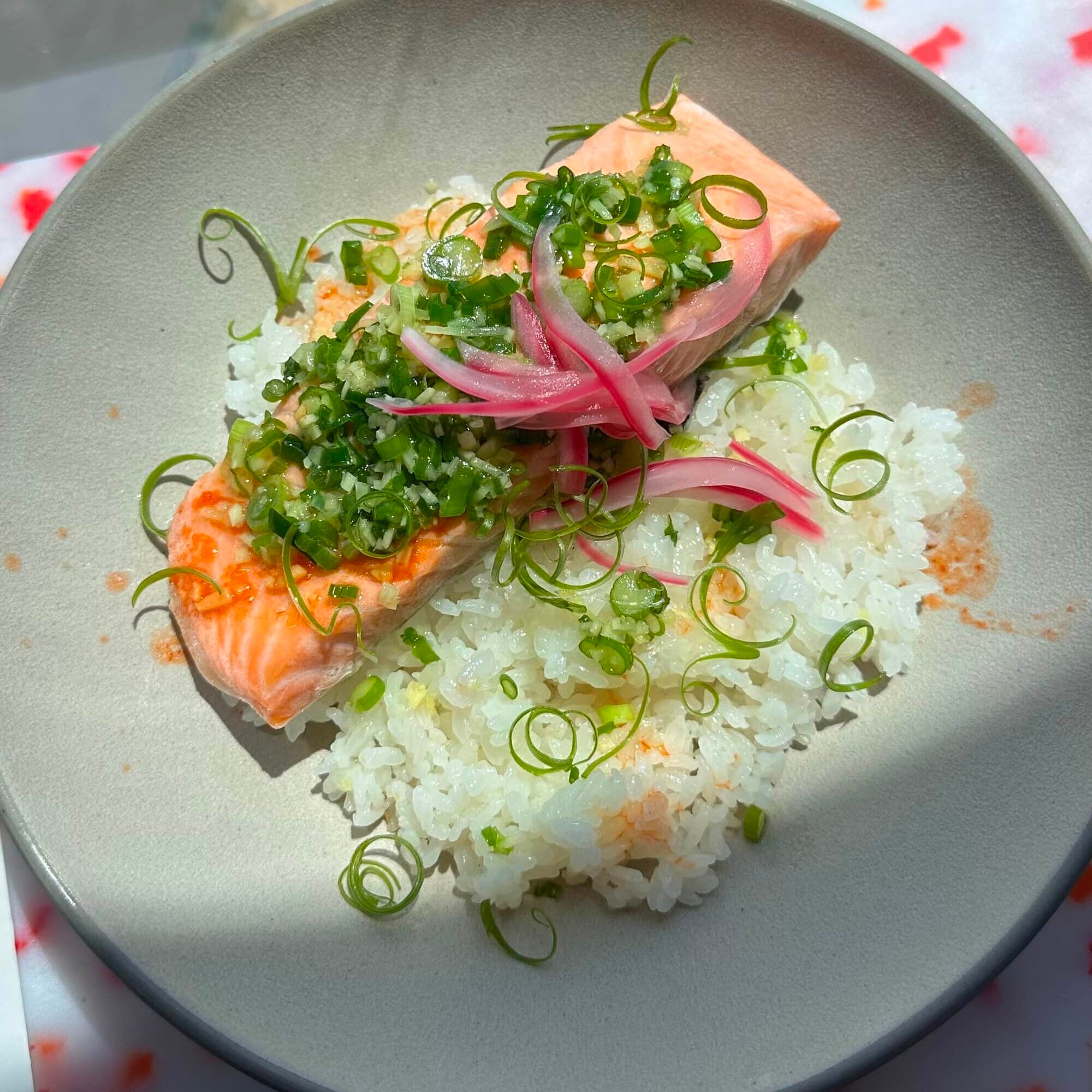 A plate of cooked salmon topped with chopped green onions and pickled red onions, served over white rice.