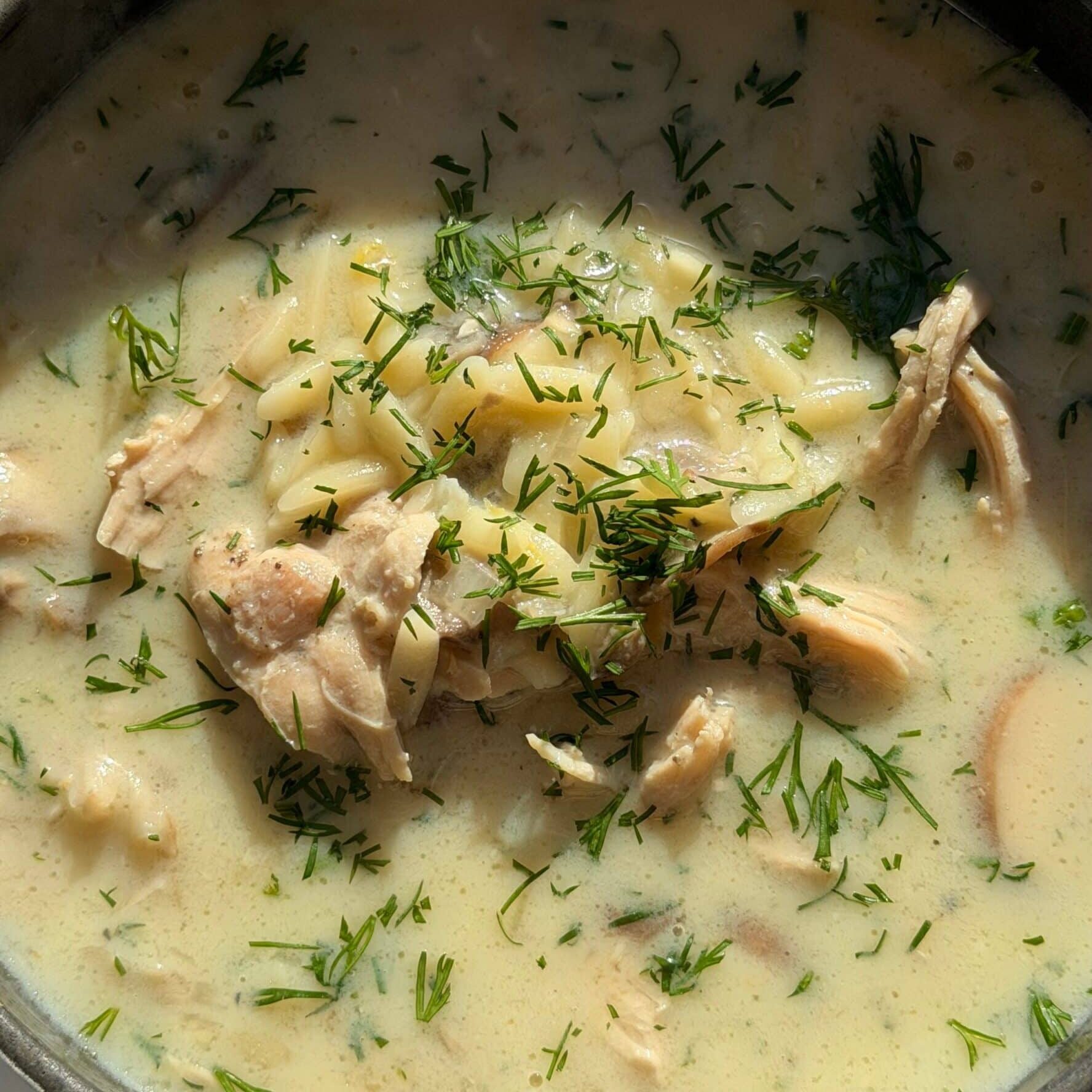 A close-up of a bowl of creamy chicken soup with chunks of chicken, potatoes, and fresh herbs visible on top.