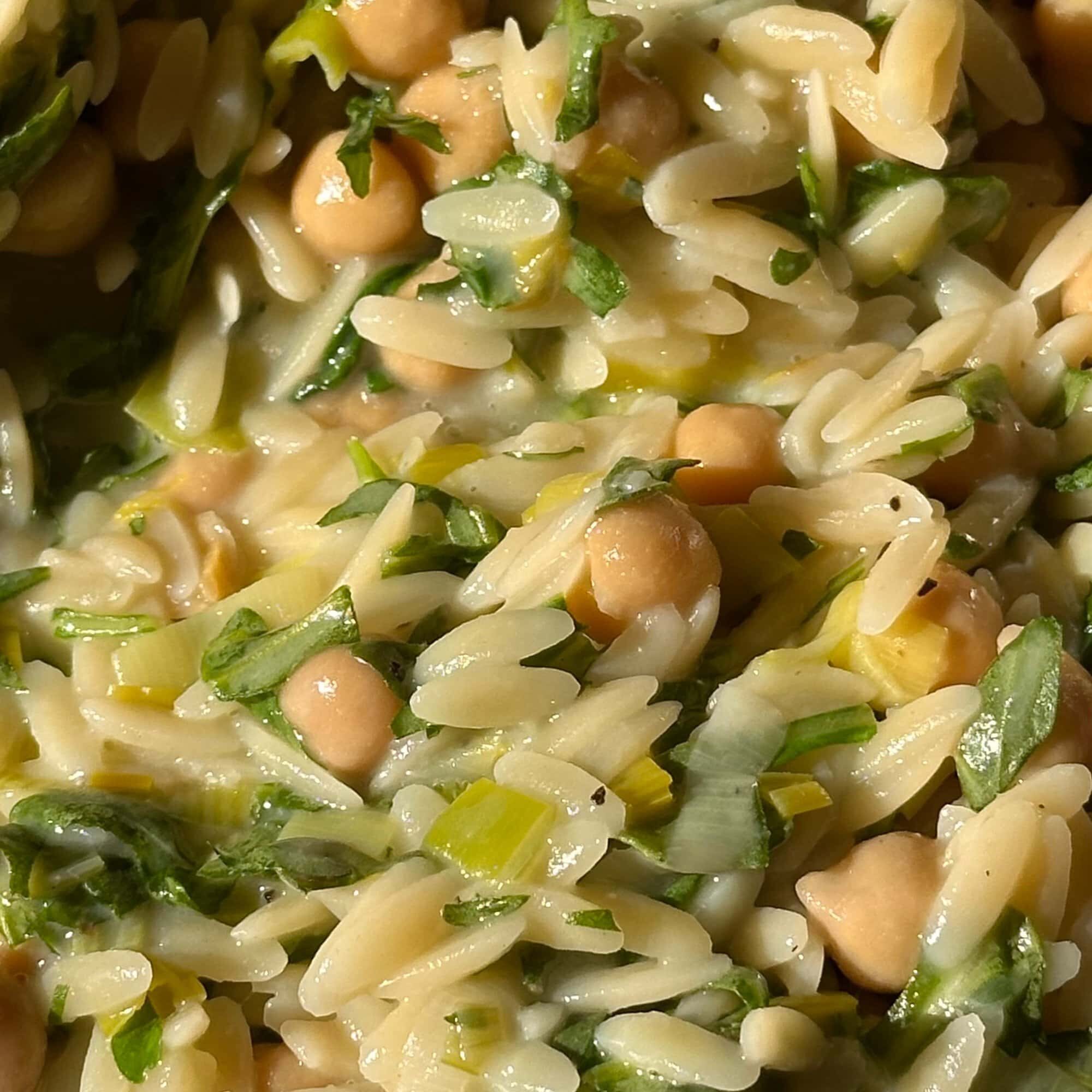 Close-up of a dish featuring orzo pasta, chickpeas, chopped greens, and herbs mixed together in a creamy sauce.