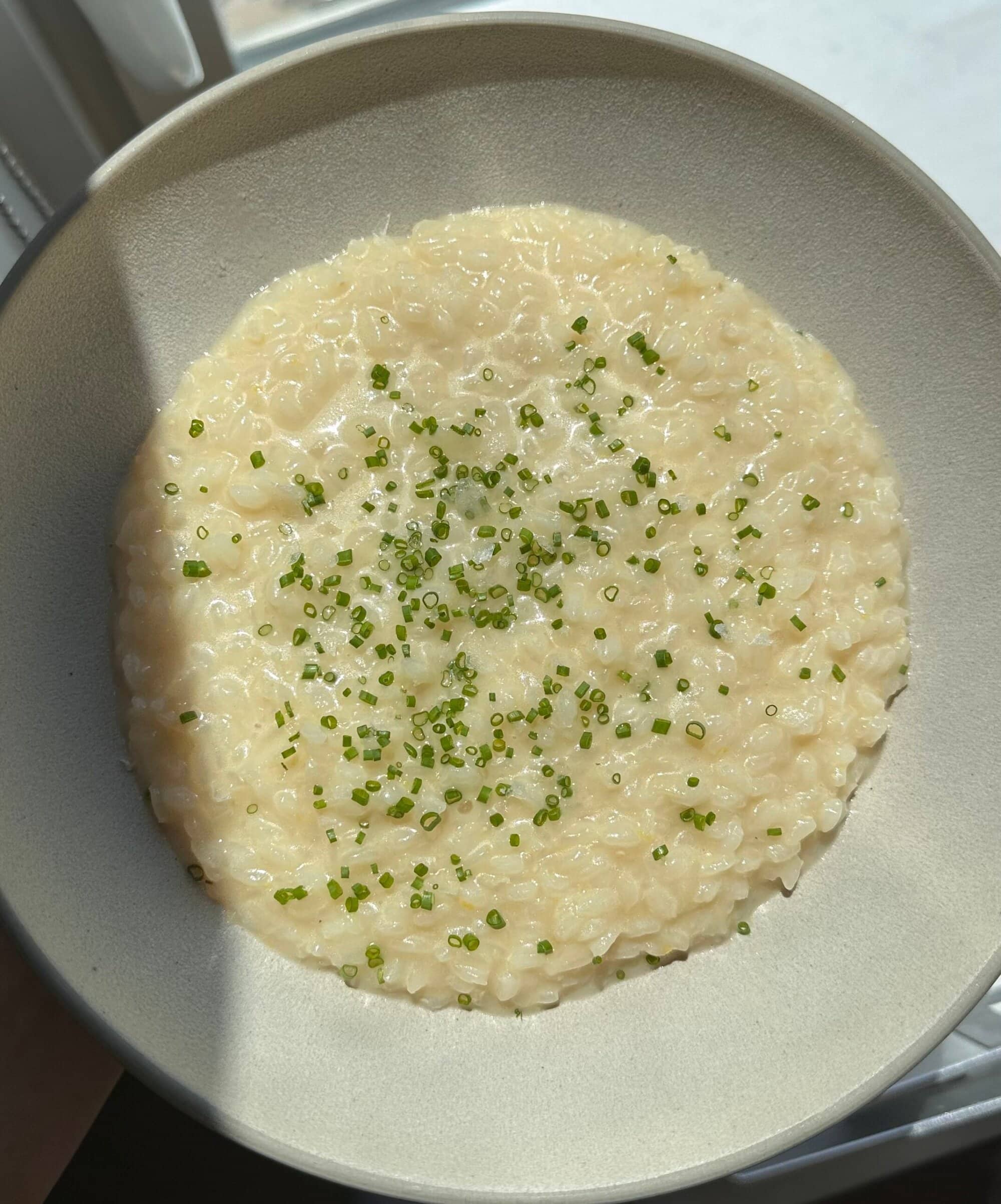 A bowl of creamy risotto topped with finely chopped chives, photographed in natural light.