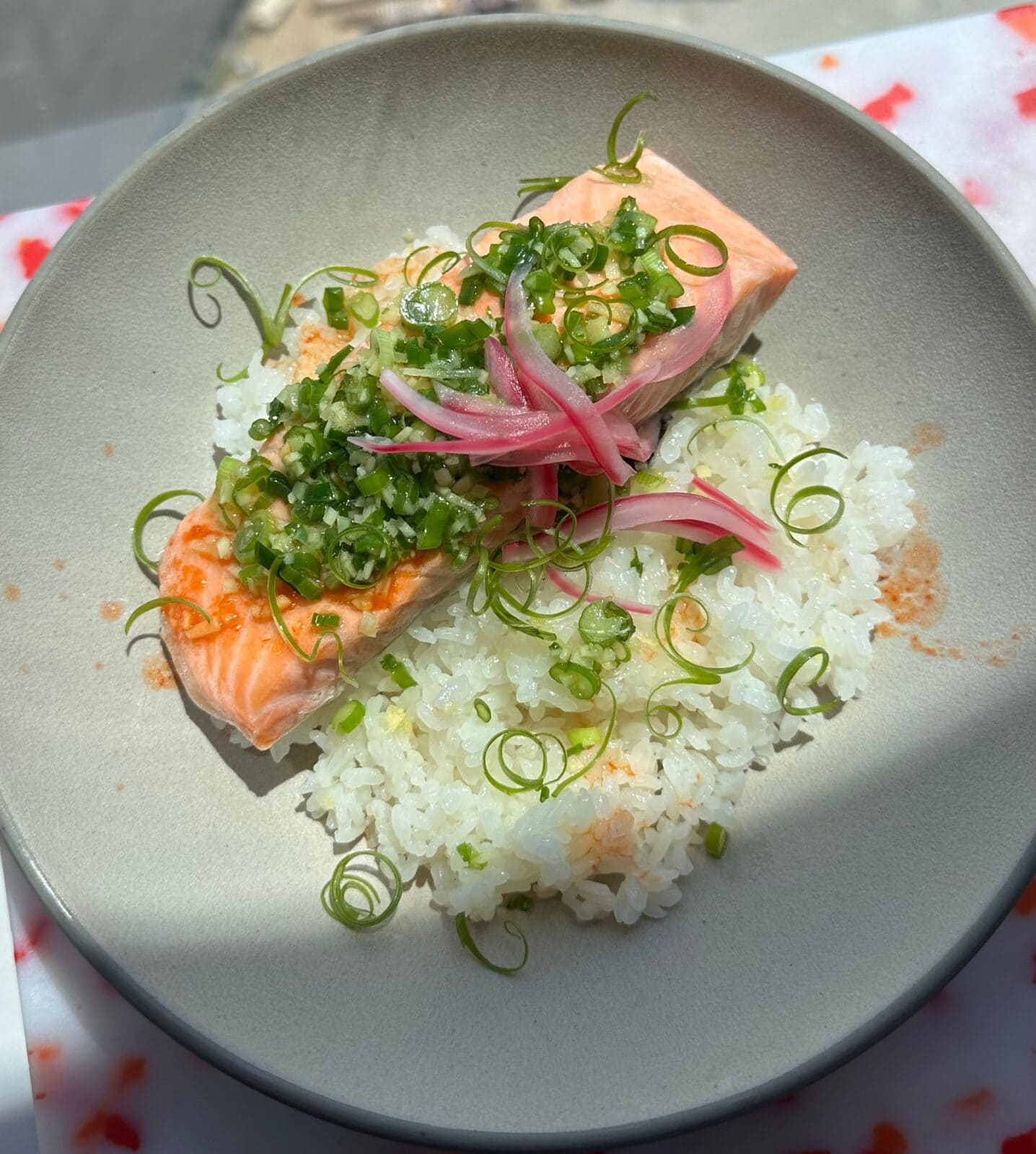 A plate of cooked salmon topped with chopped green onions and pickled red onions, served over white rice.
