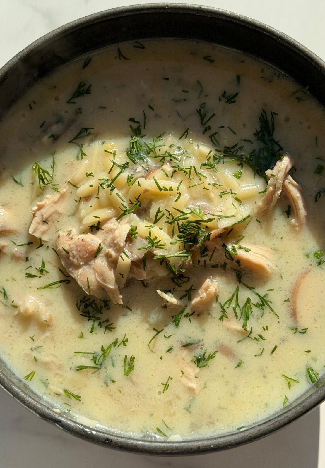 A close-up of a bowl of creamy chicken soup with chunks of chicken, potatoes, and fresh herbs visible on top.