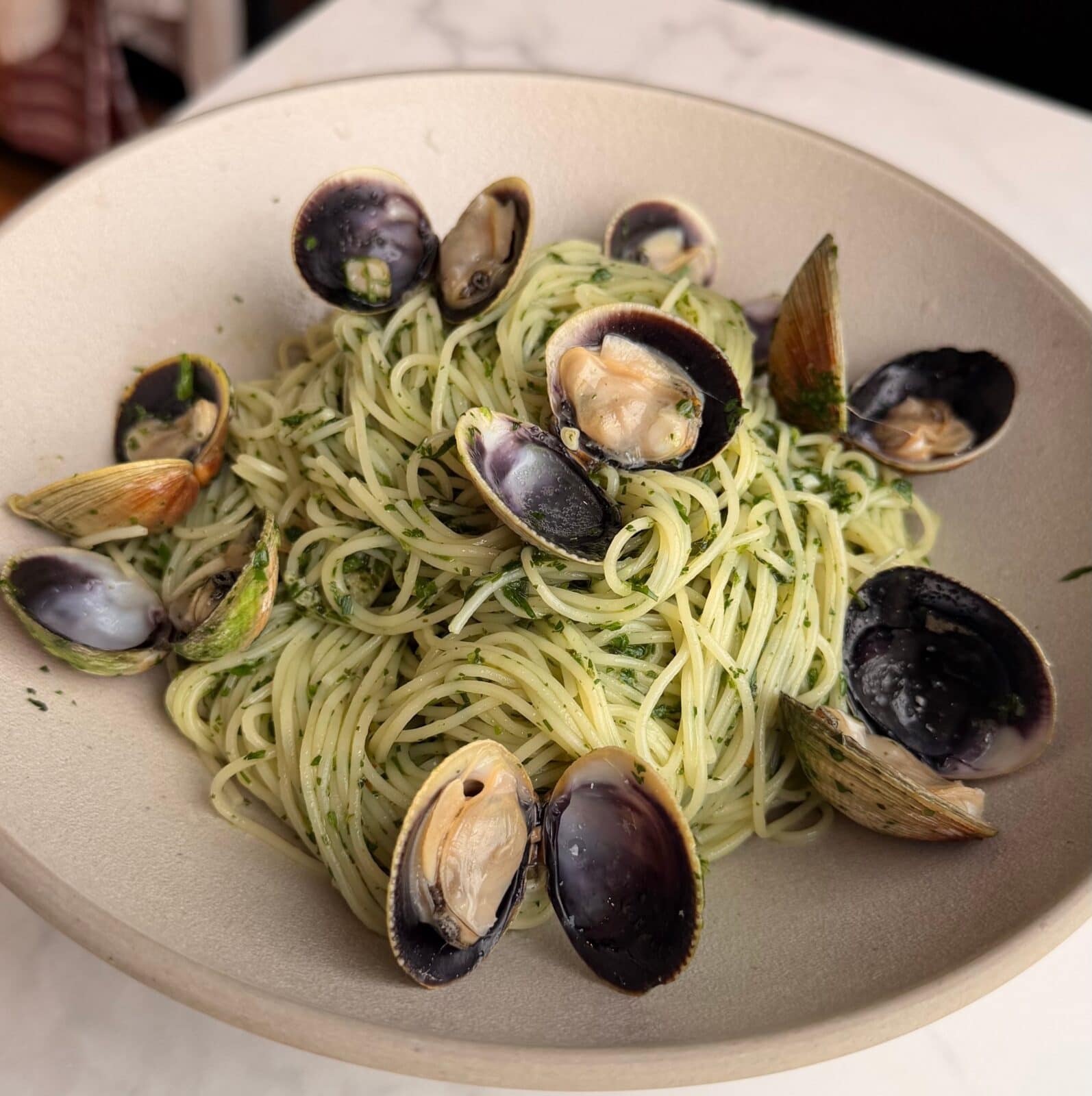 A bowl of spaghetti topped with clams in shells and garnished with chopped herbs.
