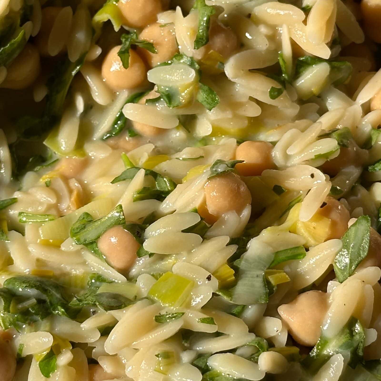 Close-up of a dish featuring orzo pasta, chickpeas, chopped greens, and herbs mixed together in a creamy sauce.