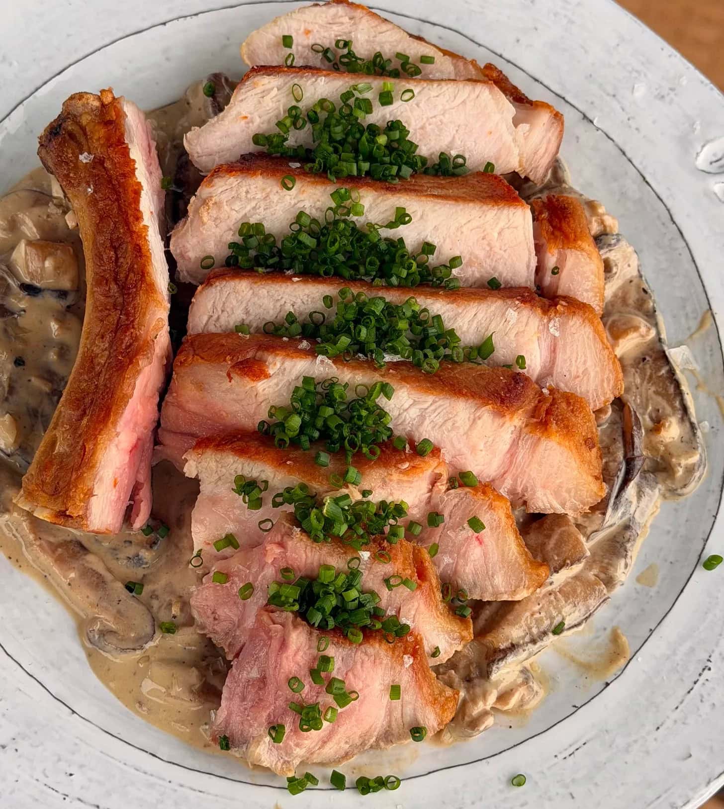 Sliced pork chop topped with chopped chives, served over a creamy mushroom sauce on a white plate.