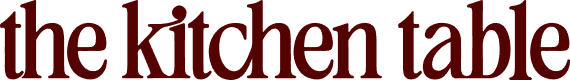 Text logo displaying the words "the kitchen table" in lowercase, bold, and serif font on a light background.